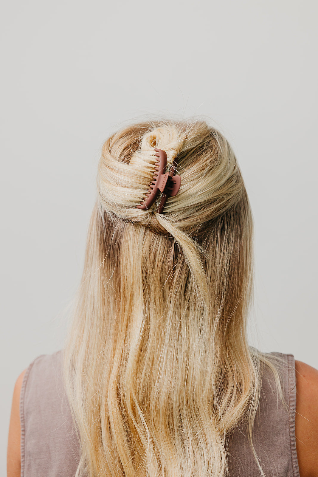 Brown matte claw hair clip holding long blonde hair in a half-up bun.