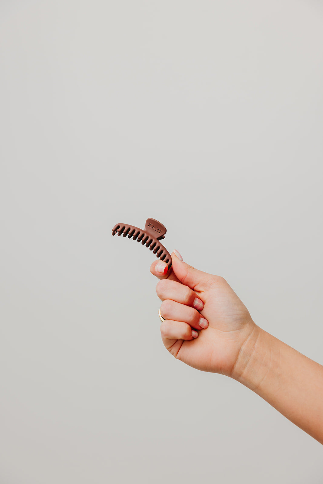 Hand holding a small dark brown matte claw hair clip with curved teeth.