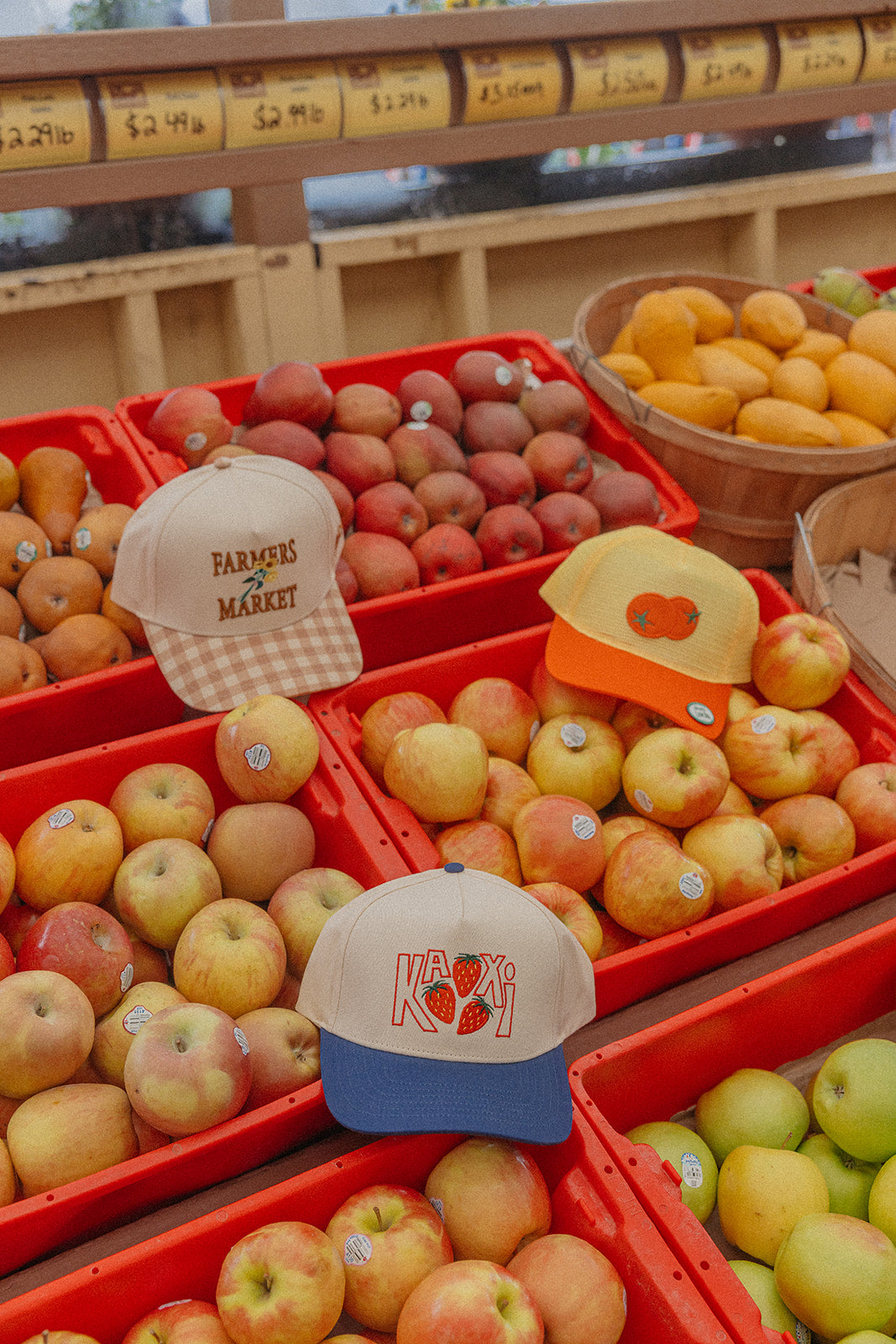 Farmers Market trucker hat with beige crown and orange gingham brim on fruit display