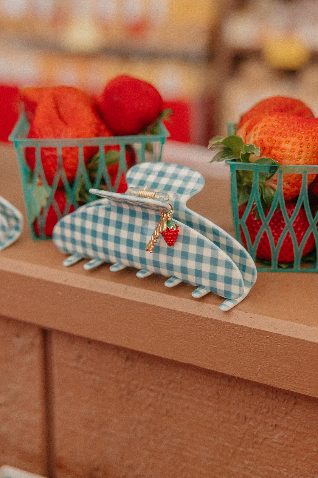 Blue gingham claw clip with red strawberry charm on a small metal hinge.