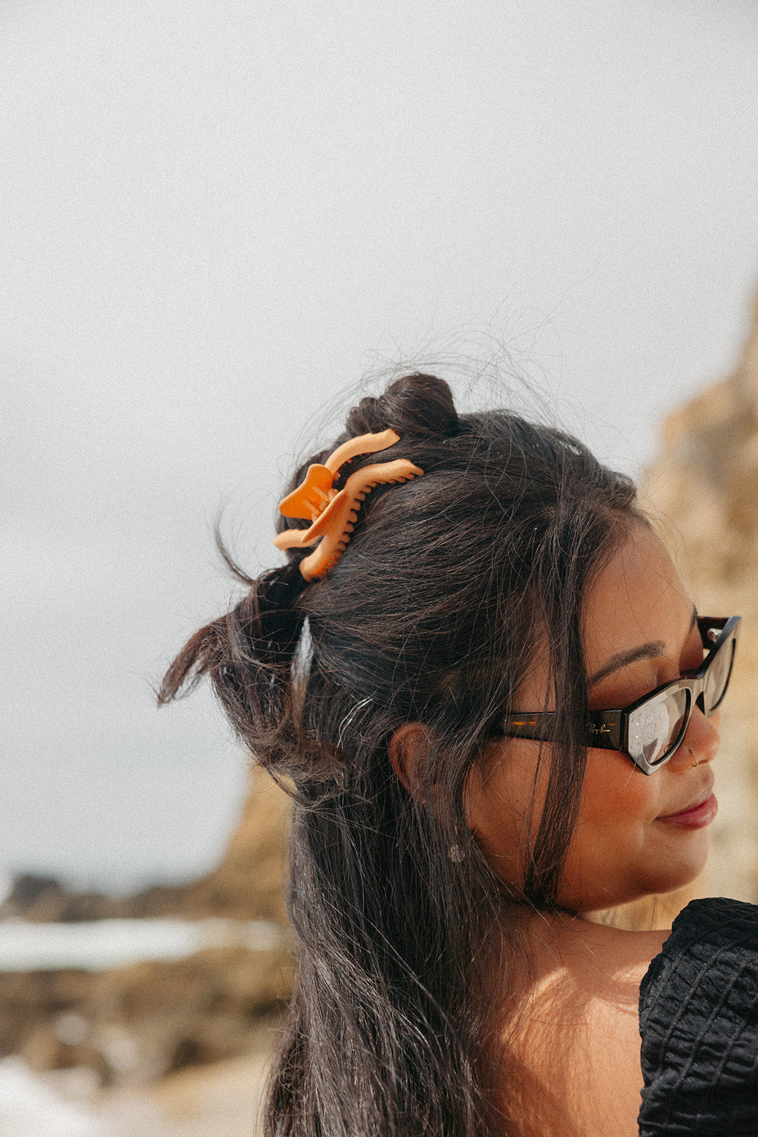 Wavy hair claw clip in warm orange, holding black hair in a high ponytail