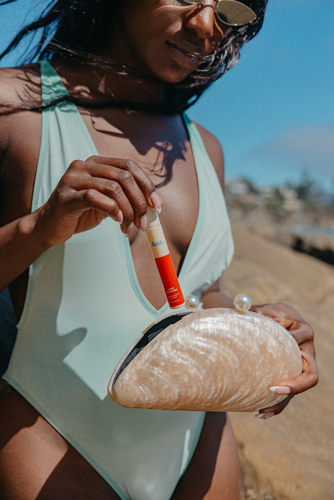 Hair perfume bottle in hand near a woman holding a white pouch