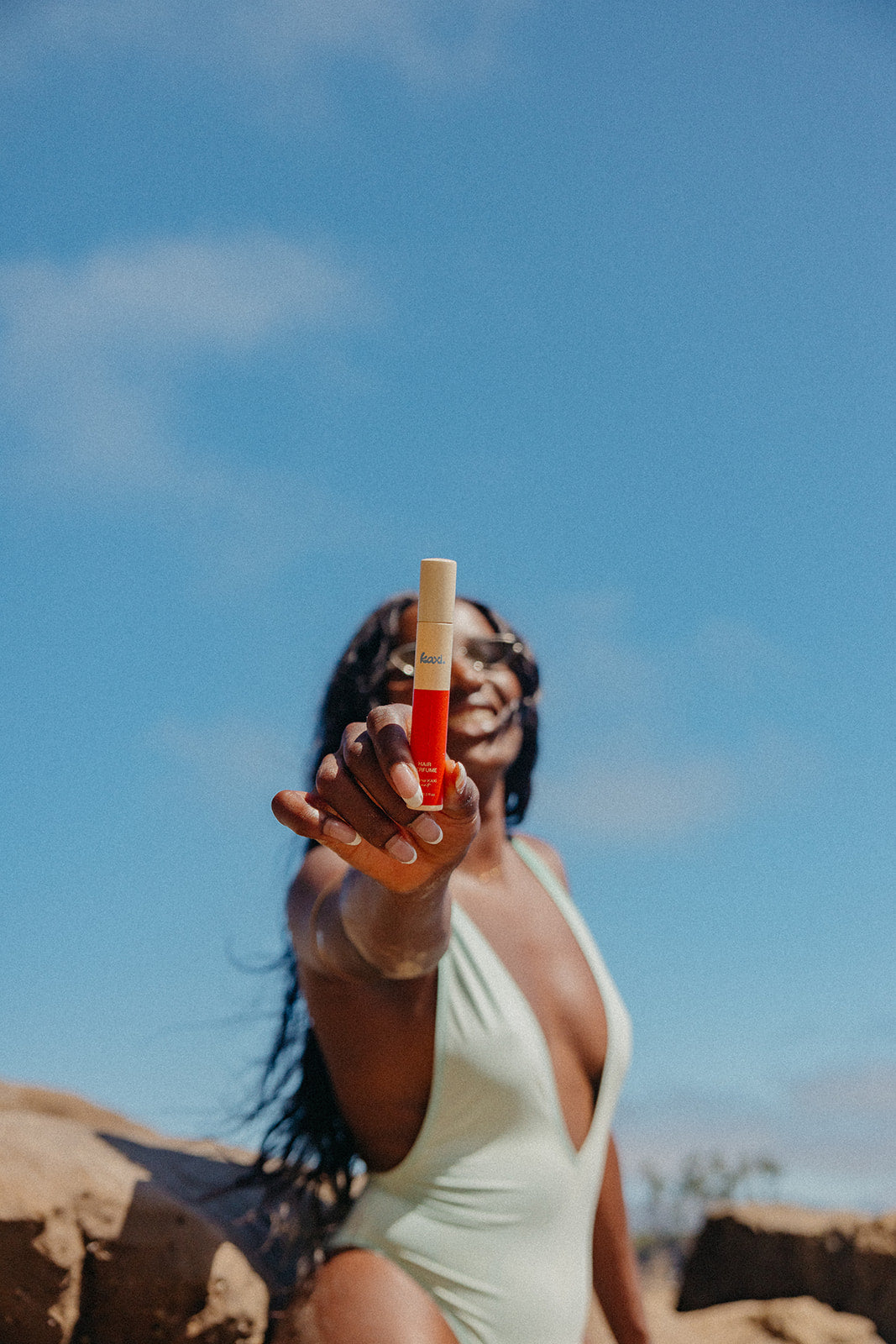 Woman holding a hair perfume spray with white top and orange label outdoors