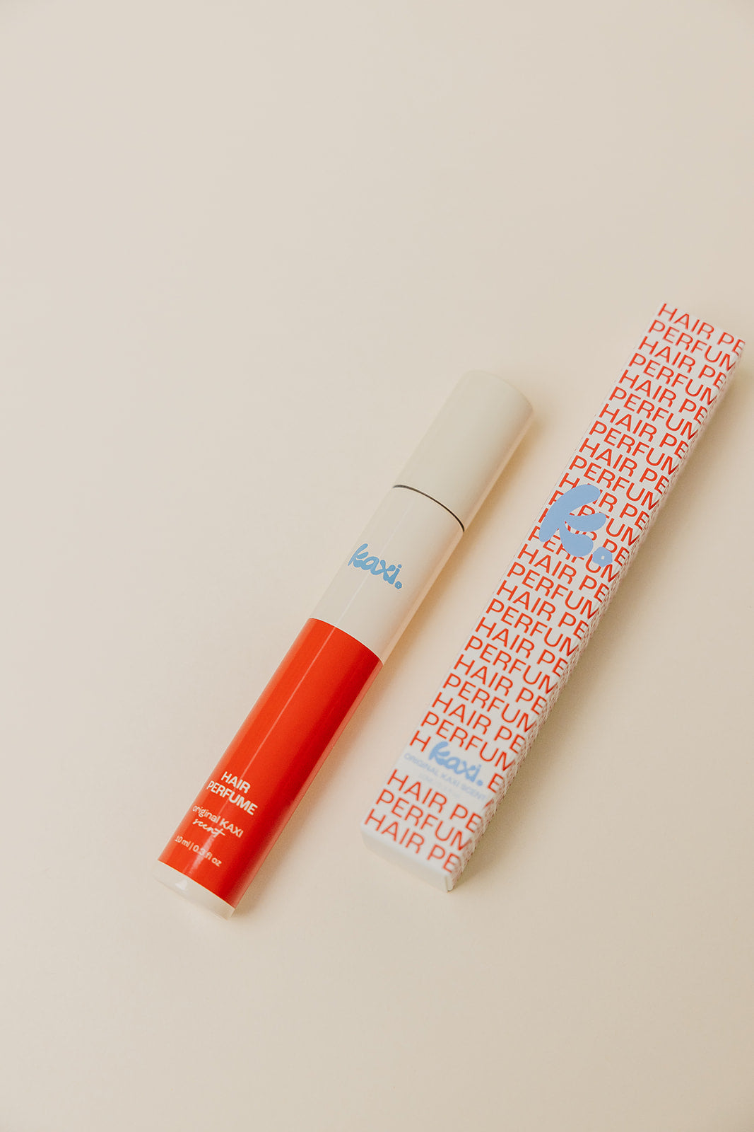 Hair perfume spray bottle lying beside a red-capped box on a light surface