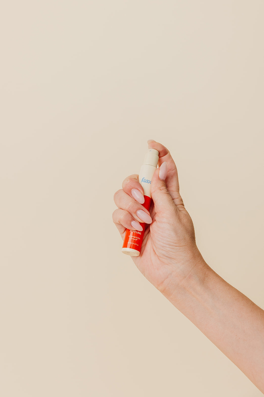 Hair perfume spray bottle held in hand, red label and cream cap