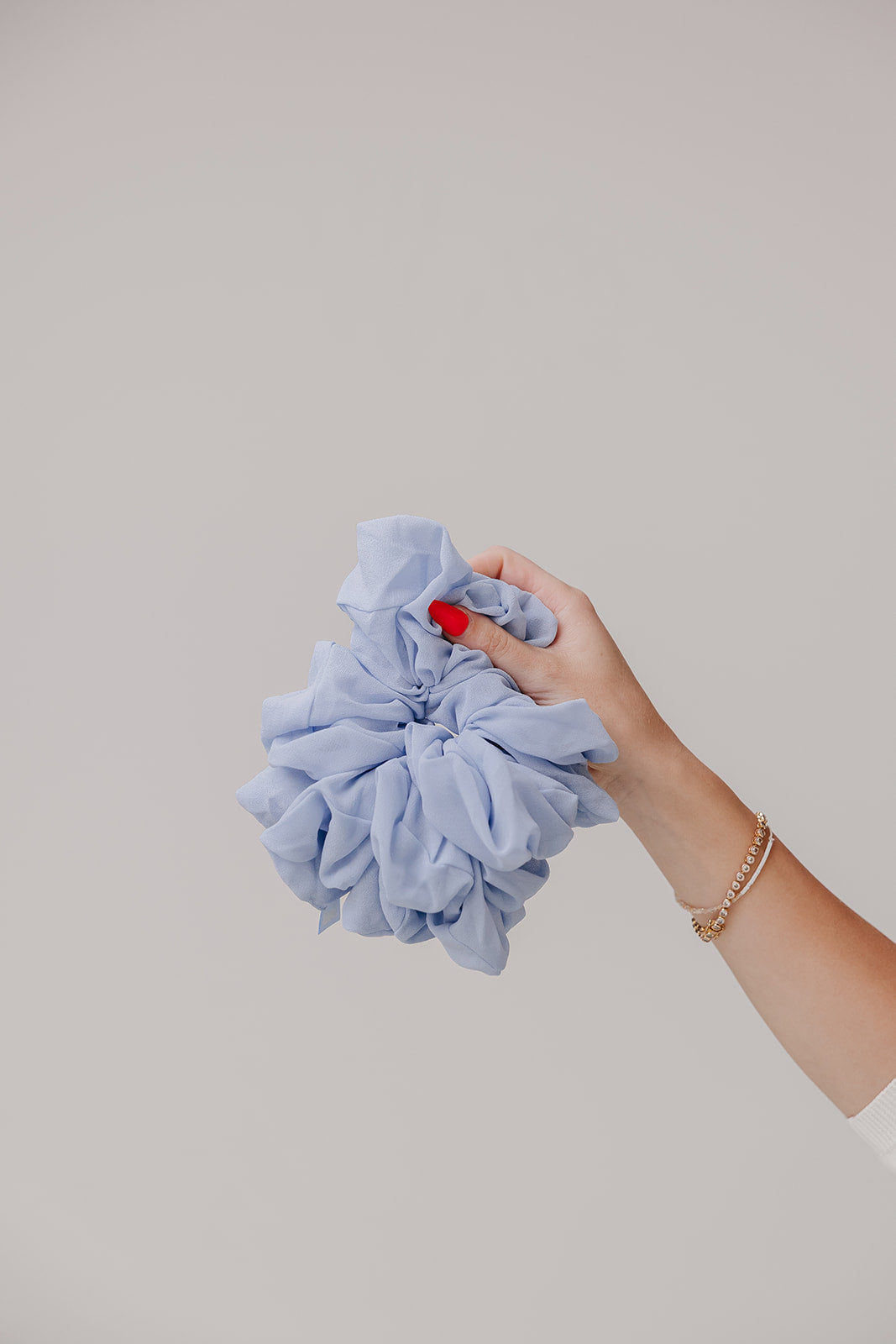 Large light blue scrunchie held in a hand, ruffled fabric.