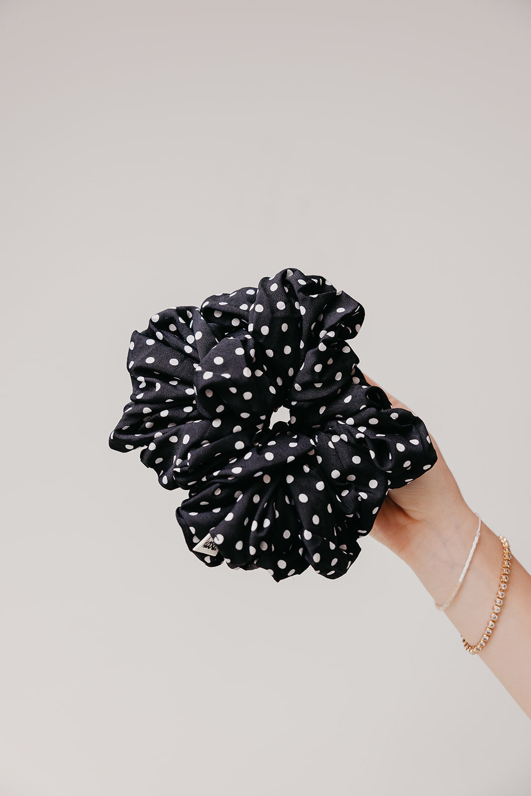 Jumbo scrunchie in black with white polka dots, held in hand.