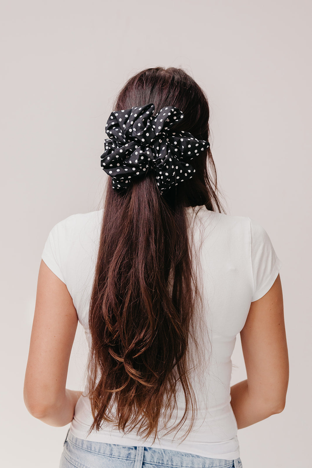 Jumbo scrunchie in black with white polka dots on long hair, back view.