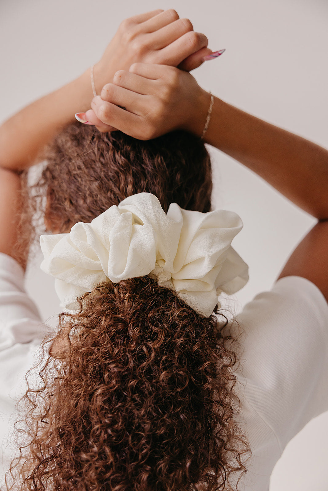 Ivory jumbo scrunchie on curly hair, hands adjusting the bun