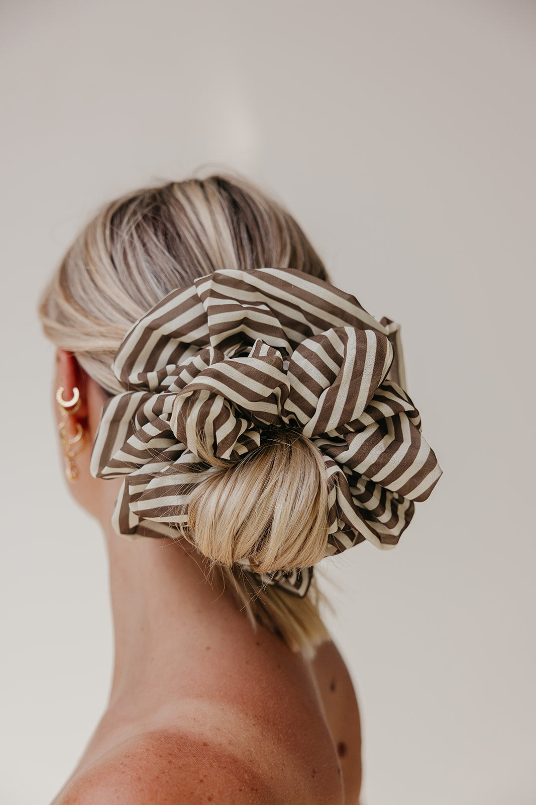 Large scrunchie with brown-and-cream striped ruffle worn in a low bun.