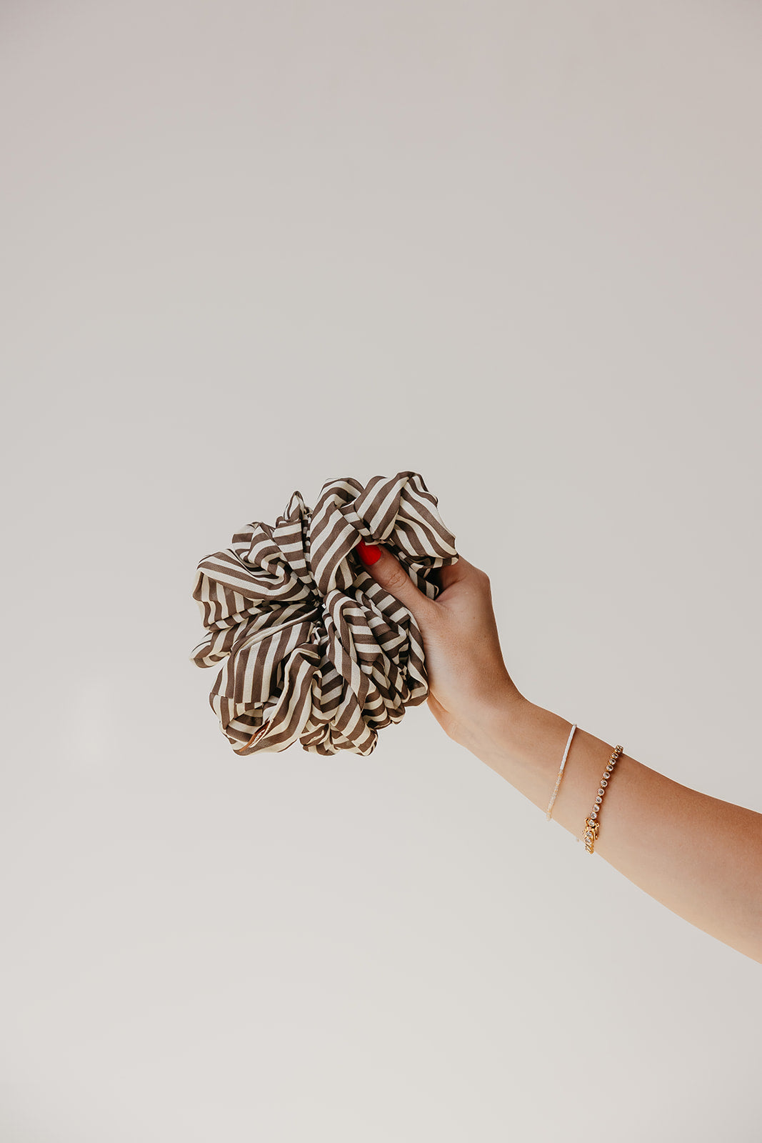 Large scrunchie with brown-and-cream striped ruffle, held in a hand.