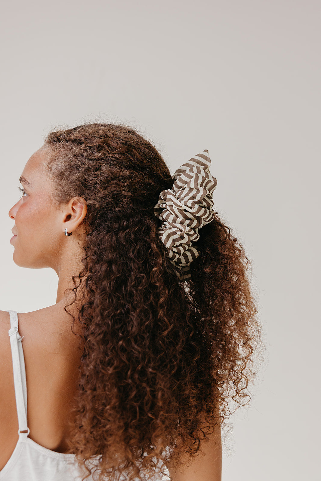 Large scrunchie with brown-and-cream striped ruffle, worn in curly hair.
