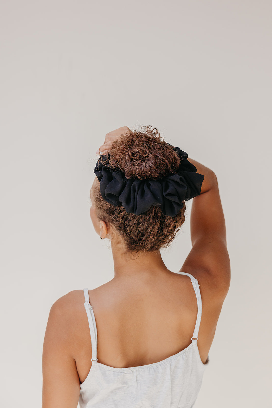 Black jumbo scrunchie on curly hair bun, viewed from the back
