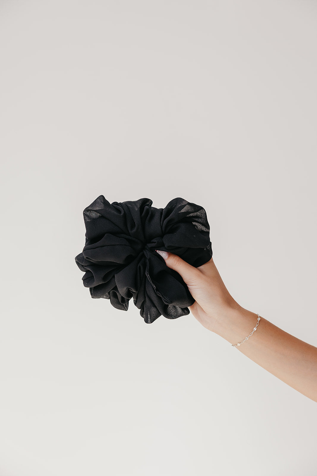 Black jumbo scrunchie held in hand, scrunched fabric detail
