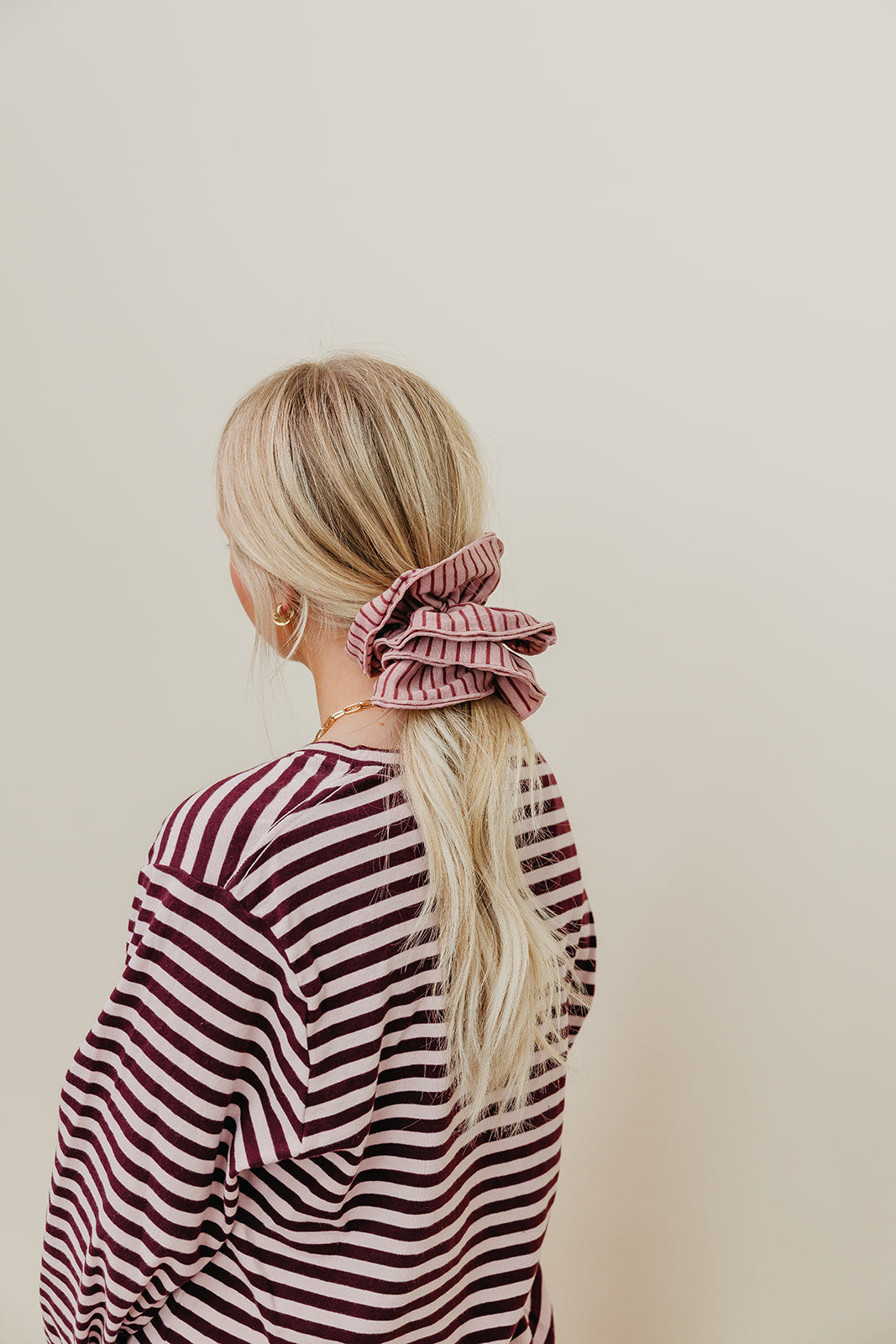 Pink and maroon striped corset-style scrunchie on blonde hair ponytail