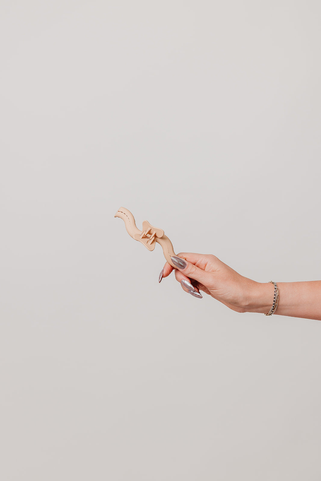 Nude wavy claw hair clip held in a hand