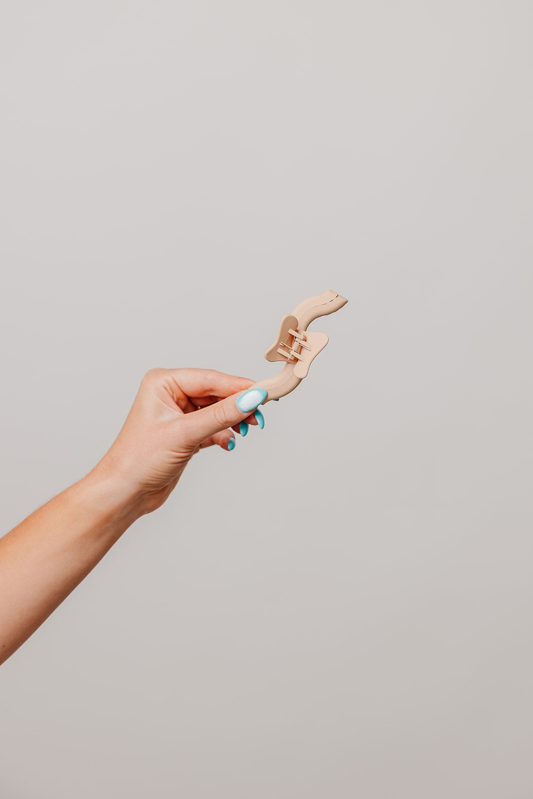 Hand holding a wavy hair claw accessory in light tan