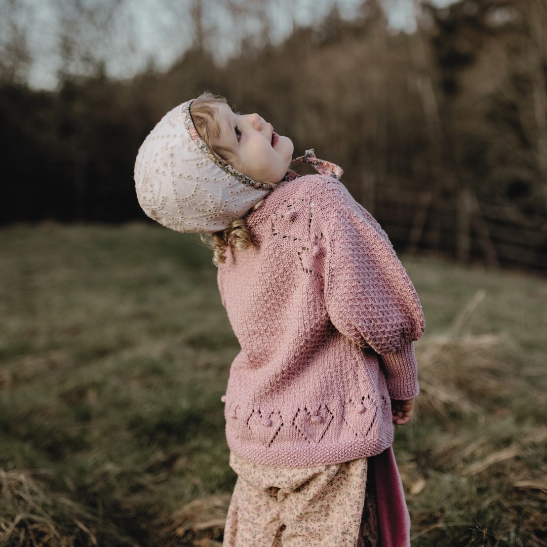 Light pink knit cardigan with button front and diamond pattern, long sleeves.