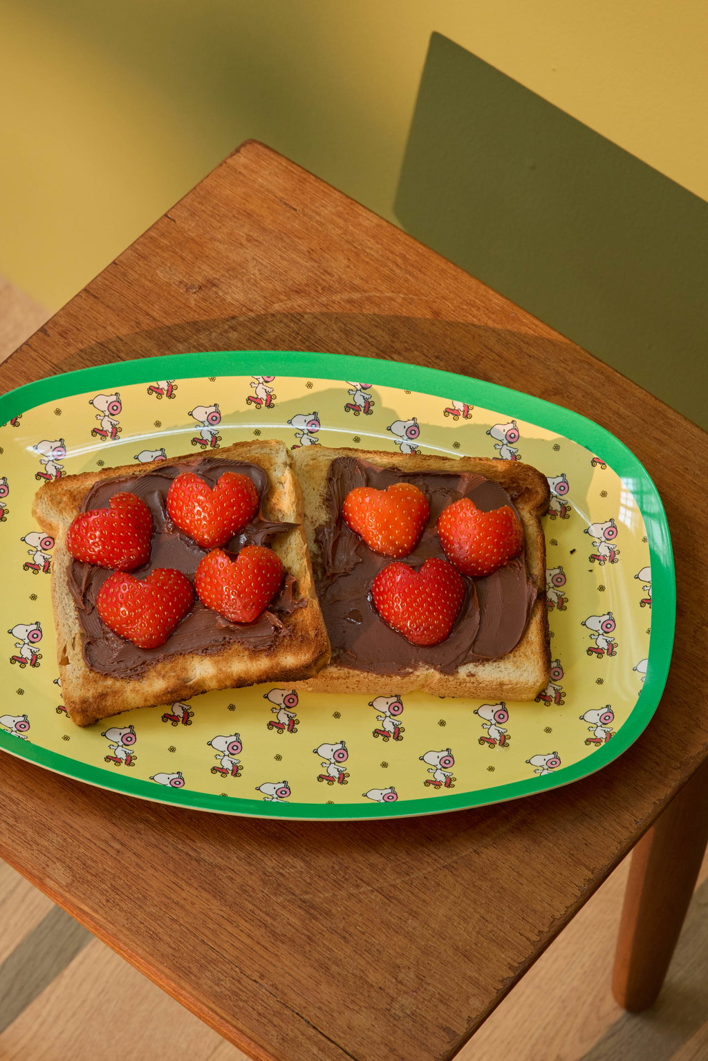 Yellow oval Snoopy print plate with green edge, holding toast and strawberries