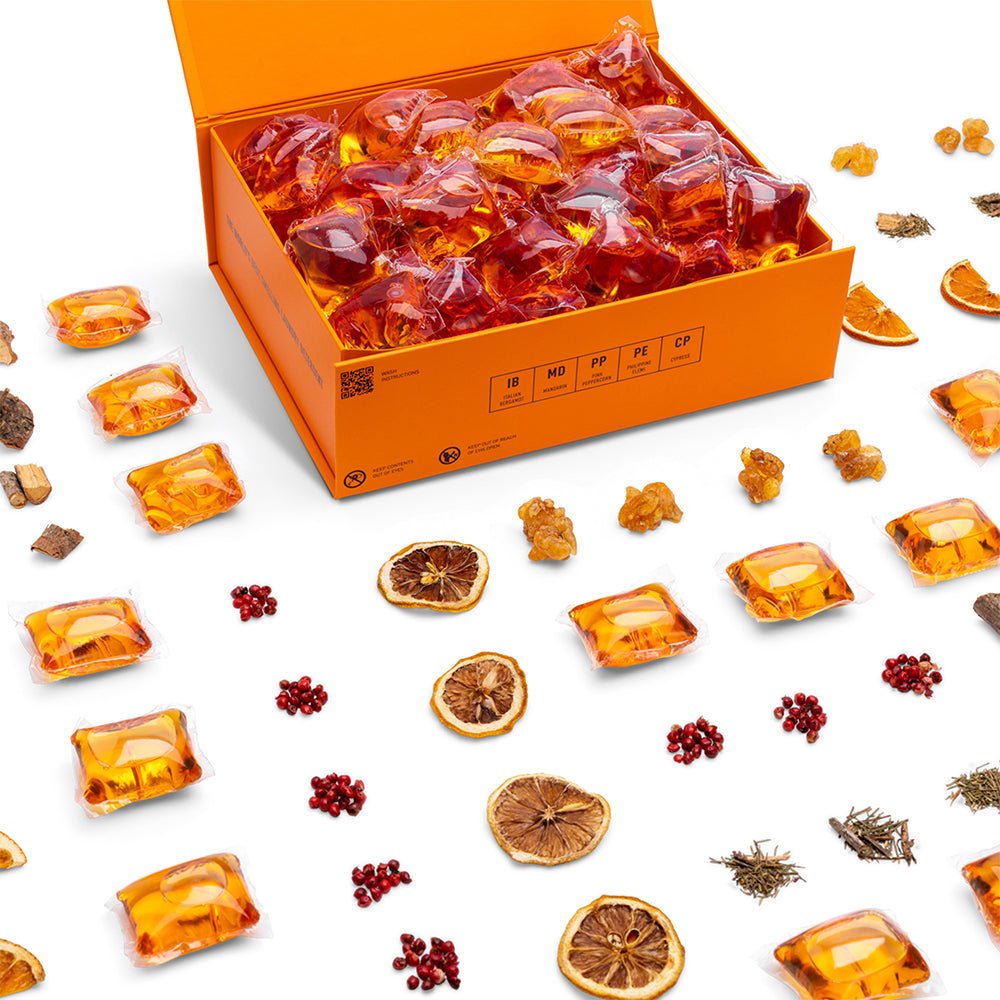 Open orange box of laundry detergent pods with scattered amber wrapped pod pieces