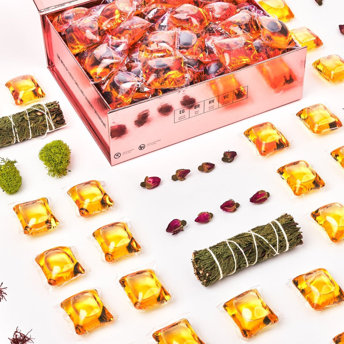 Laundry detergent pod box close-up with orange gel pods and dried botanicals around