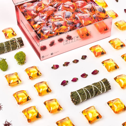 Laundry detergent pod box close-up with orange gel pods and dried botanicals around