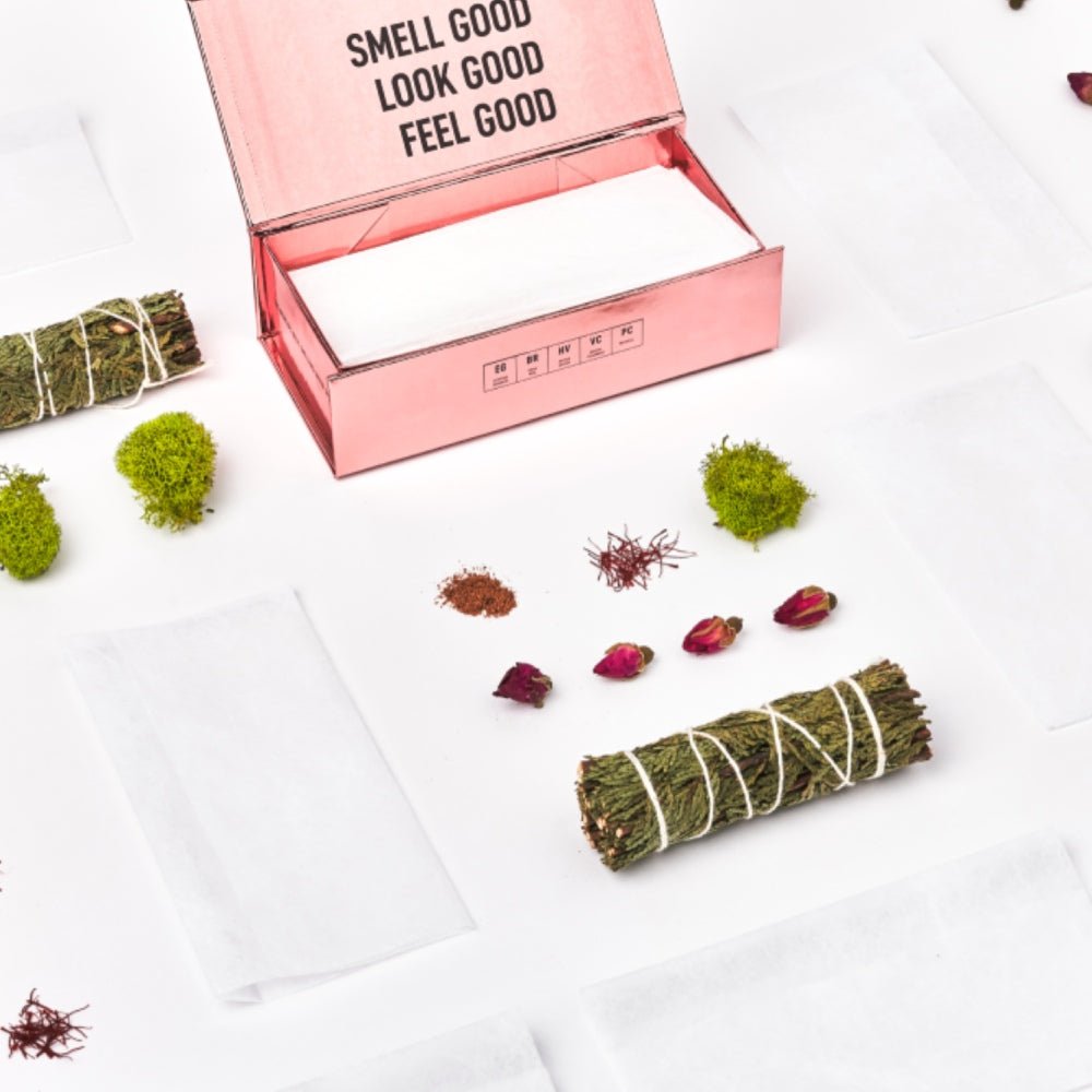 Open pink scented dryer sheet box with white sheets and scattered herbs and petals