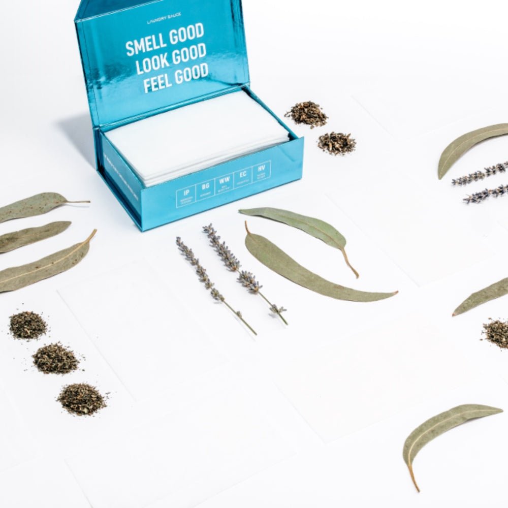 Luxury scented dryer sheets with a blue open box and white sheets, plus scattered dried botanicals.