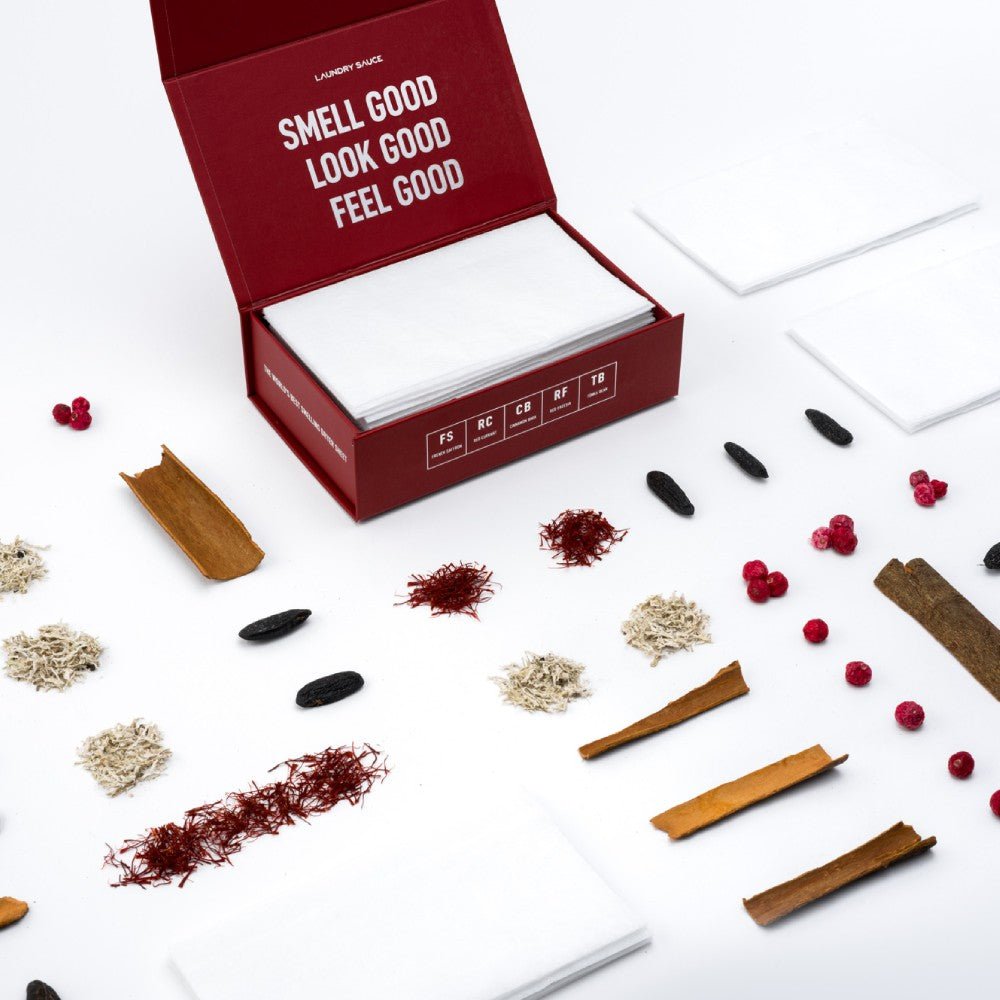 Open deep red scented dryer sheet box with white sheets and scattered spices and botanicals