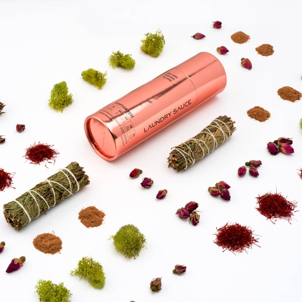 Coral laundry scent booster tube on flat lay with scattered botanicals around