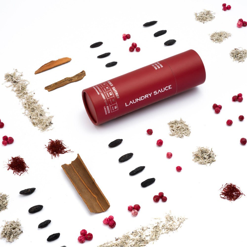 Dark red laundry scent booster tube with spices and dried botanicals scattered around
