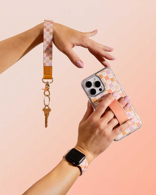 Phone case with peach bow pattern and tan strap, held in one hand