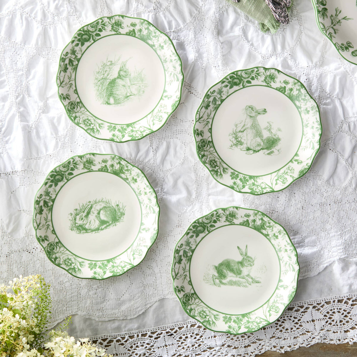 Four green-and-white Easter rabbit plates laid out, each with floral border and scalloped rim