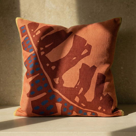 Orange throw pillow with oversized brown leaf sketch and blue speckled stripe