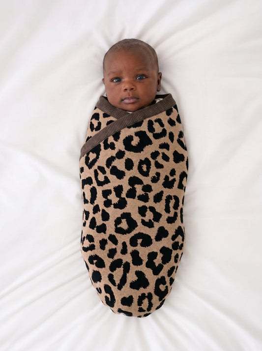 Leopard jacquard knit baby blanket swaddling a baby, with dark spot pattern and trim