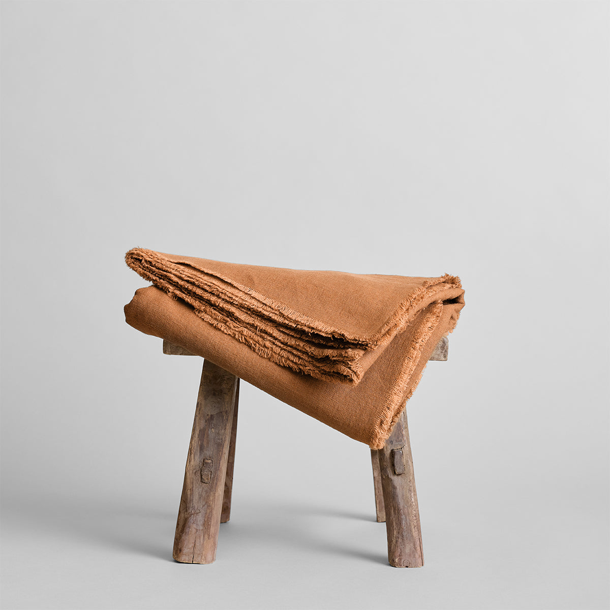 Rust-brown fringed linen tablecloth folded on a wooden stool