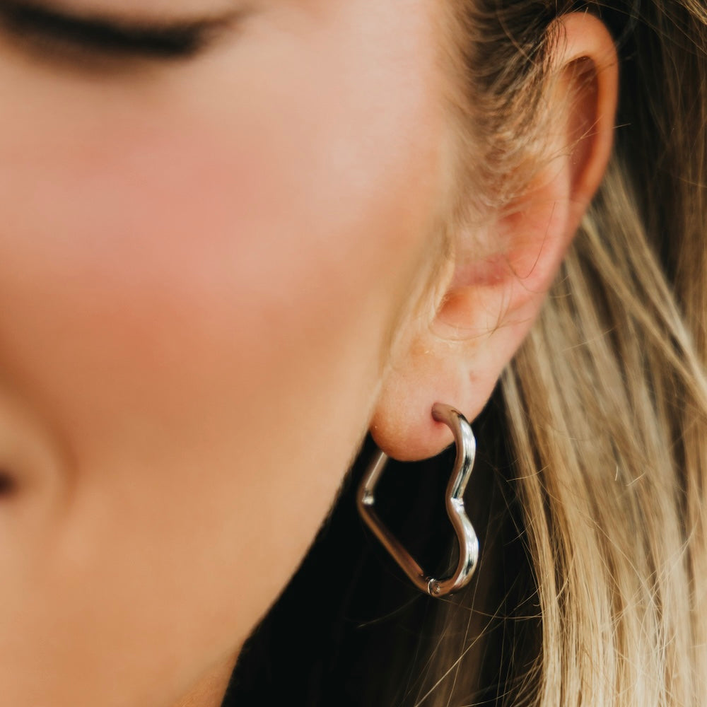 Silver-tone heart hoop earrings with open heart shape and hinged closure.