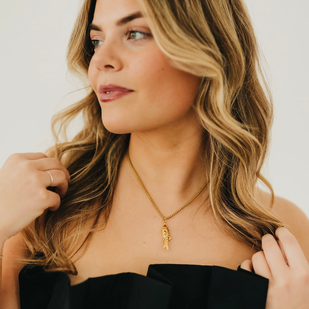 Gold-tone lucky fish pendant necklace with fine chain, worn at the neckline