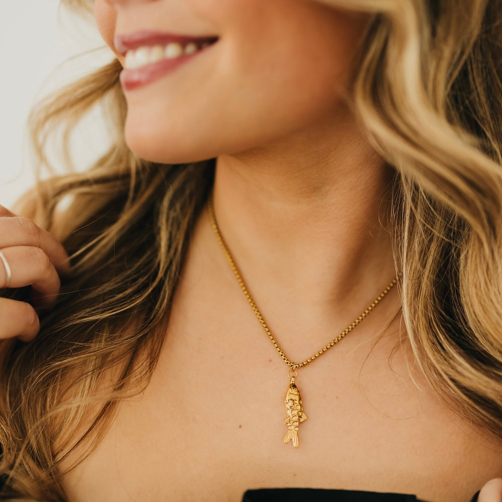 Gold-tone fish charm pendant necklace on fine chain, detailed close-up