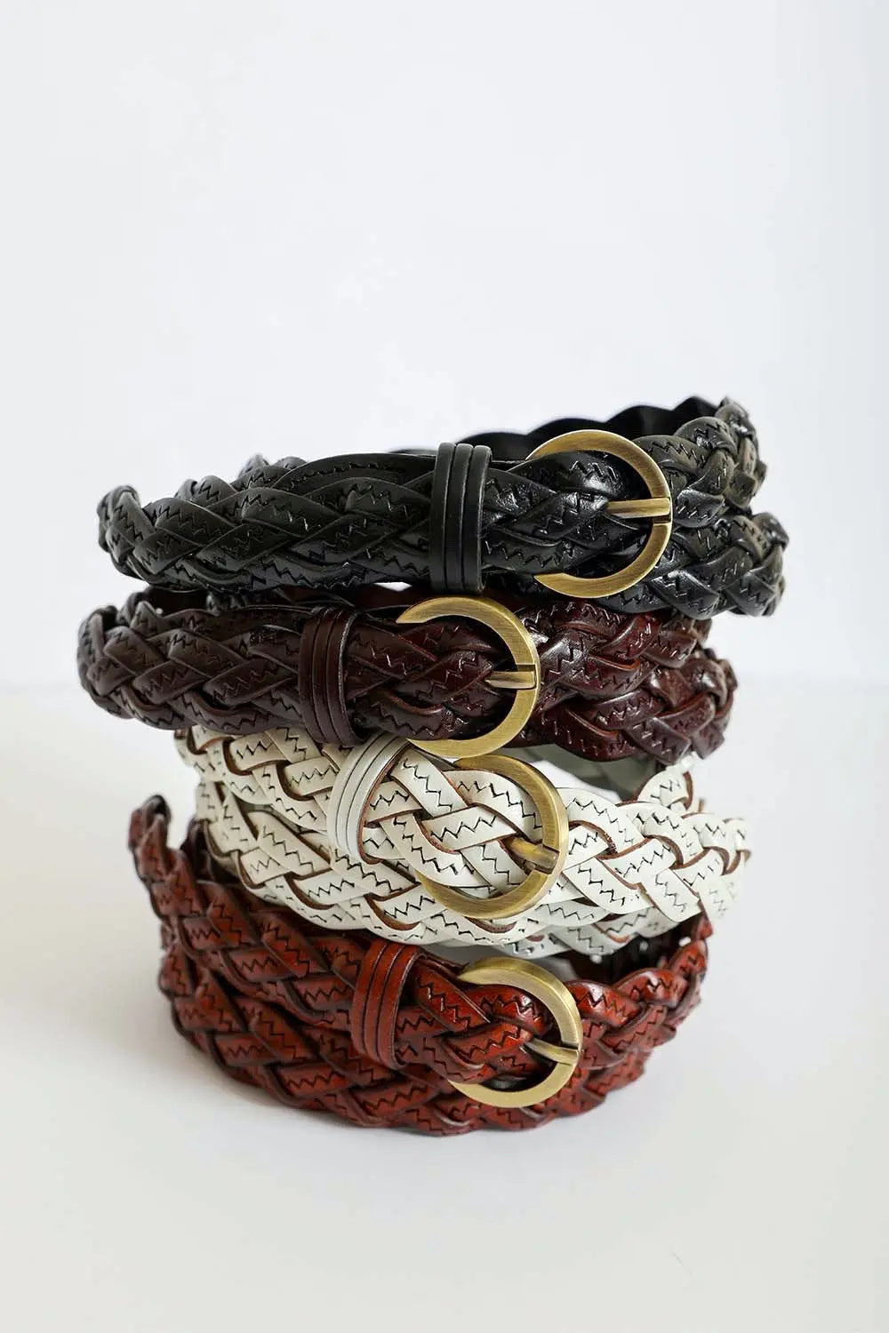 Stack of braided leather belts in black, brown, white, and rust tones with gold buckles