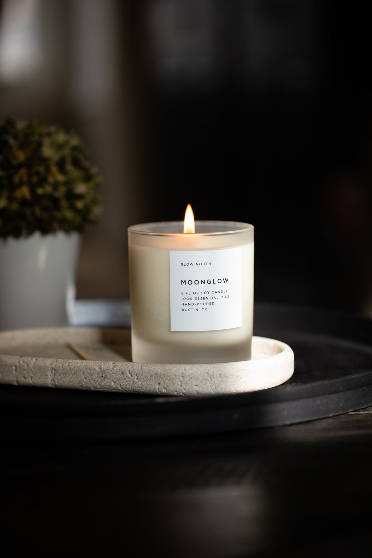 Lit Moonglow signature candle in a frosted glass jar with a white label.
