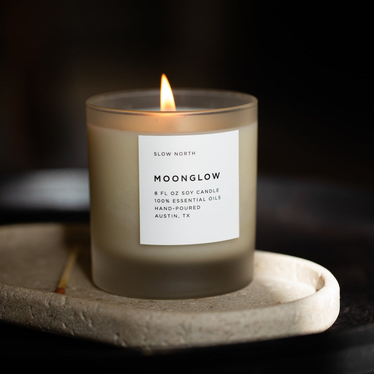 Moonglow signature candle in a frosted glass jar, lit, with a white label.