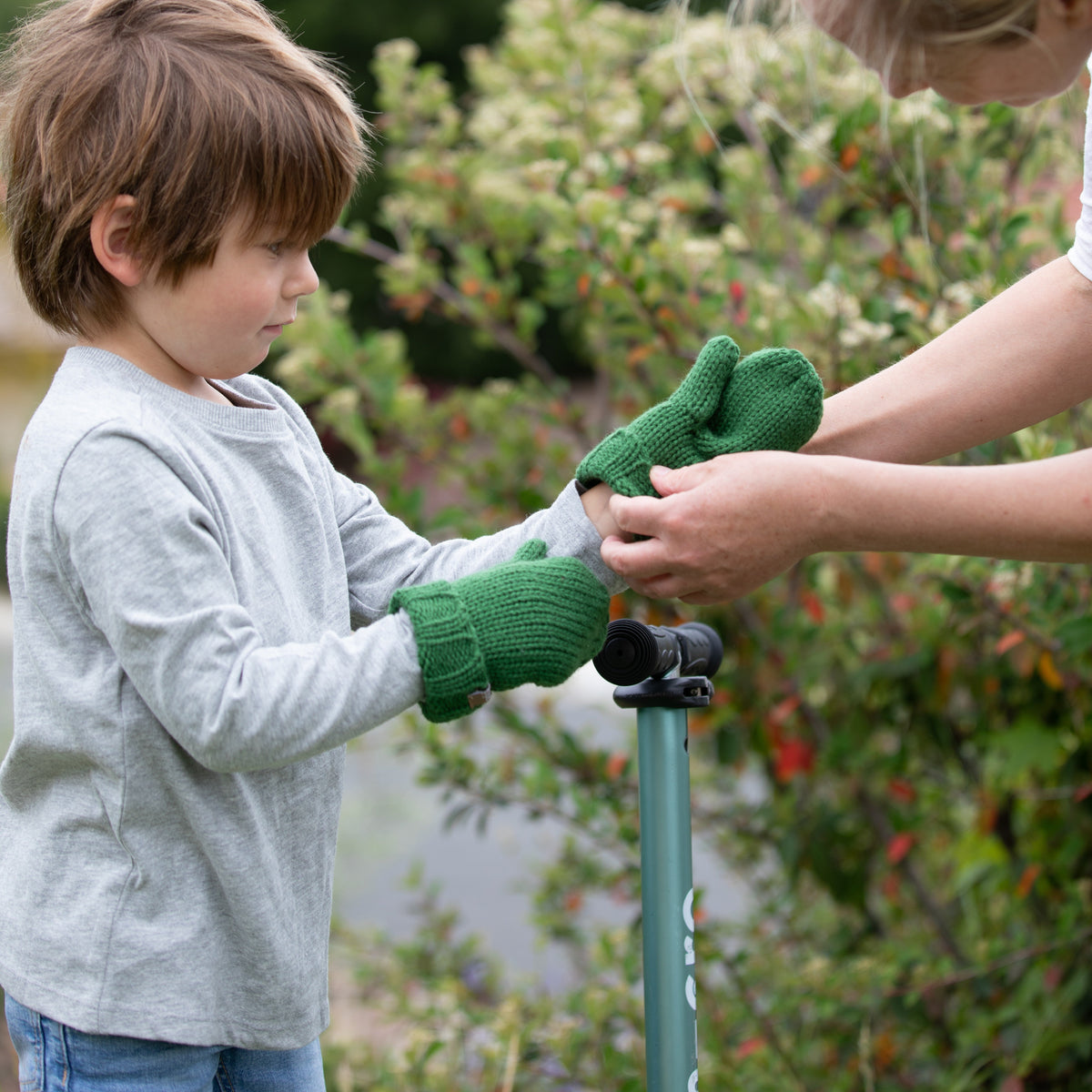 Green knit mittens being put on a child's hands