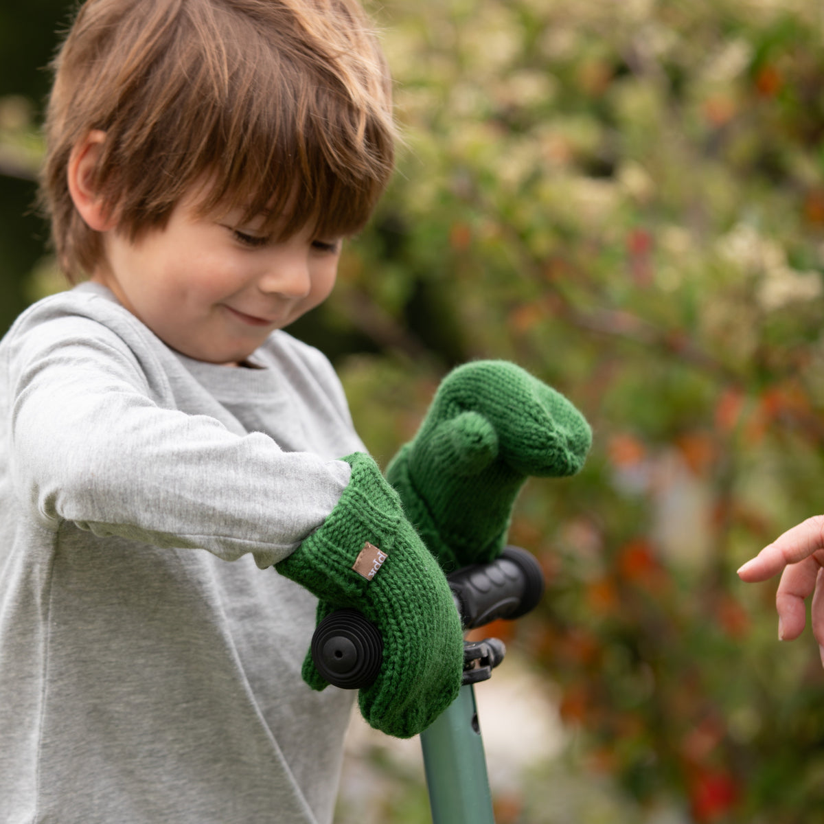 Green knit mittens worn by a child at a scooter handlebar