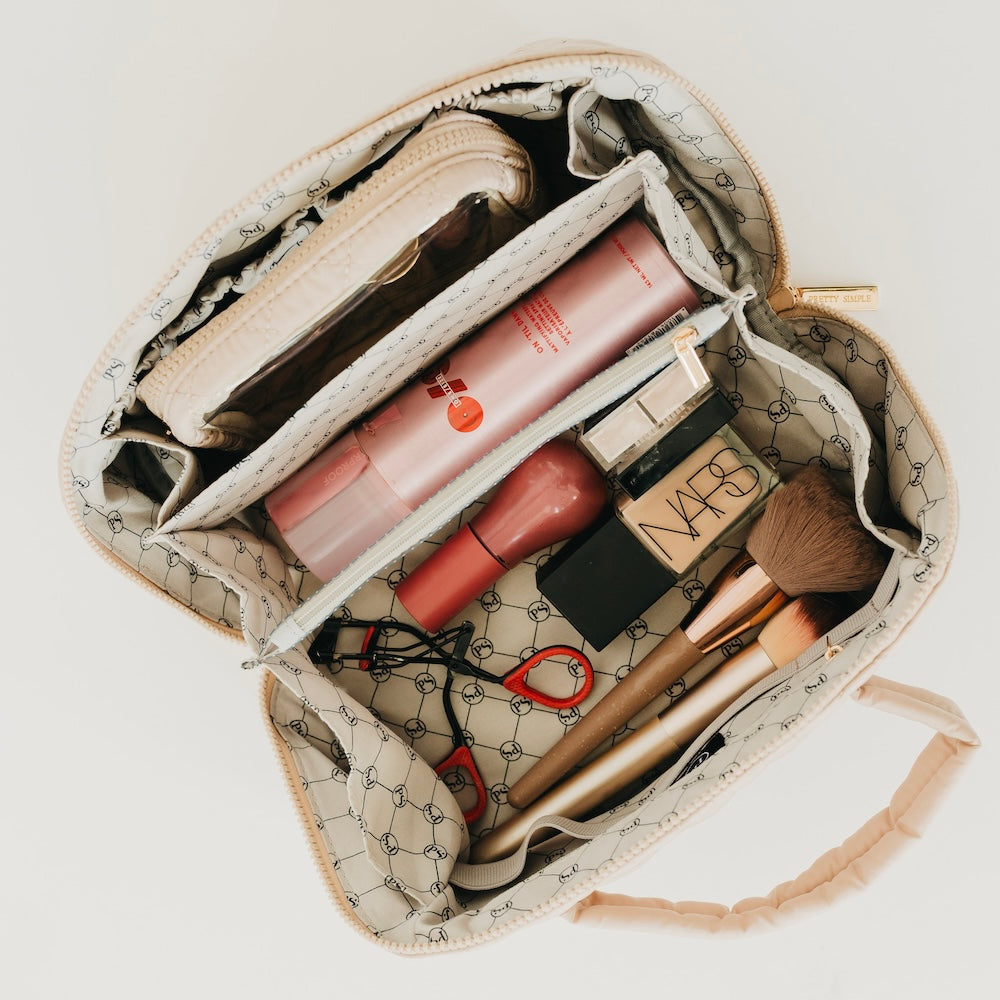 Taupe quilted cosmetics bag interior with makeup organizer pockets and stacked items.