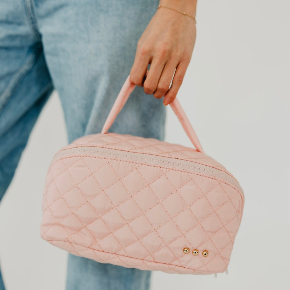 Pink quilted cosmetics bag with patterned stitching and gold-tone stud logo on front.