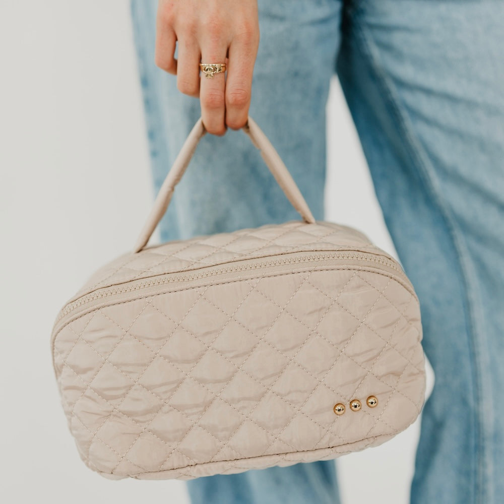 Taupe quilted cosmetics bag with top zipper and gold-tone double stud front detail.