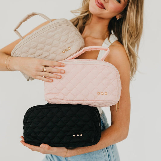 Pink quilted cosmetics bag with top zip and gold-tone stud accents, holding handle.