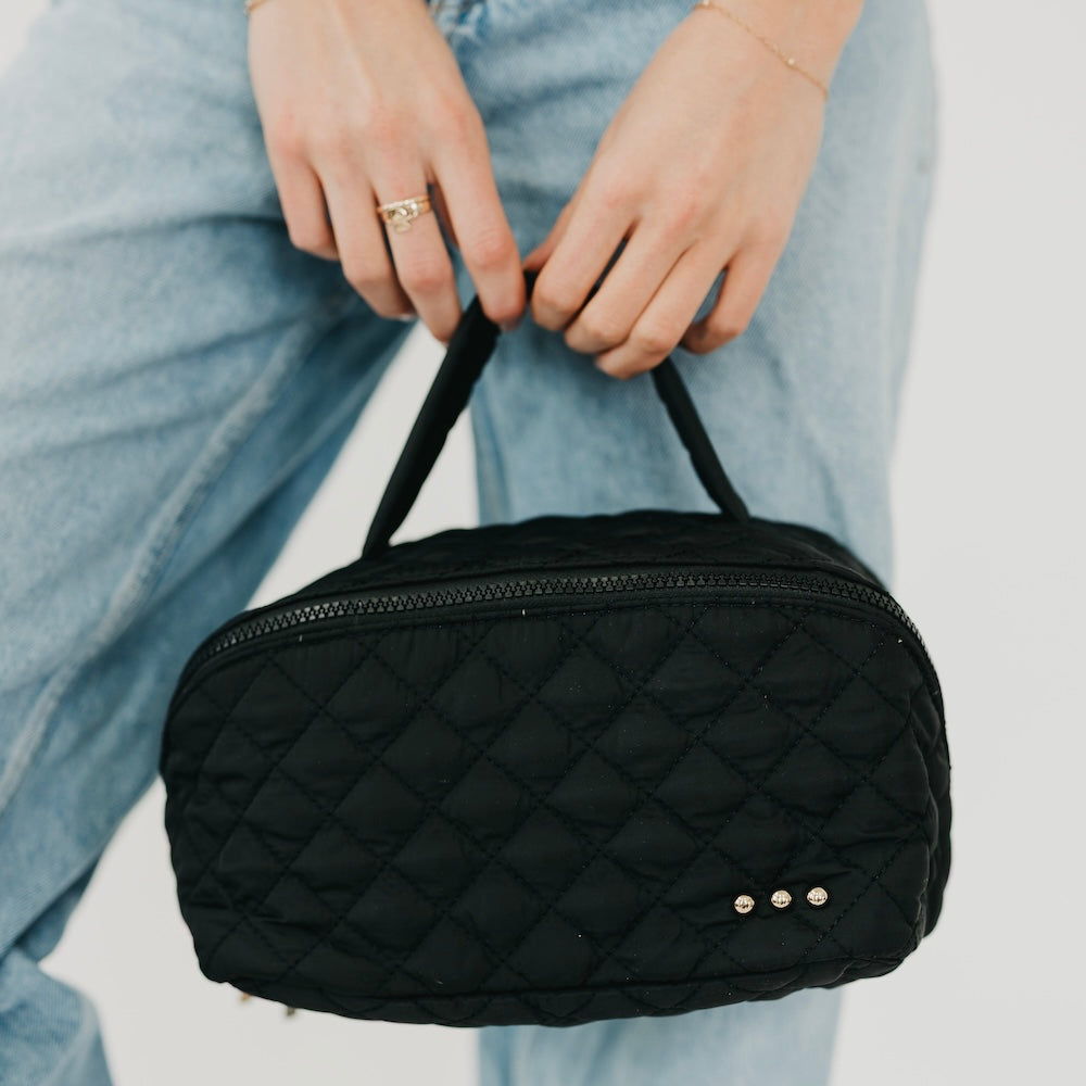 Black quilted cosmetics bag with top zip, diamond stitching, and gold-tone stud detail.