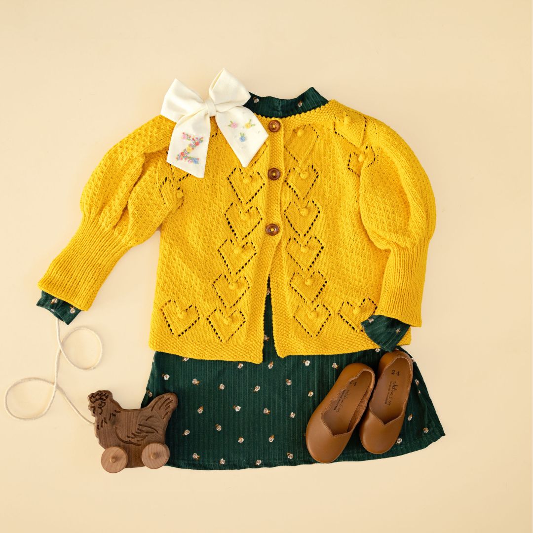 Light mustard knit cardigan with button front, diamond pattern, and long sleeves.